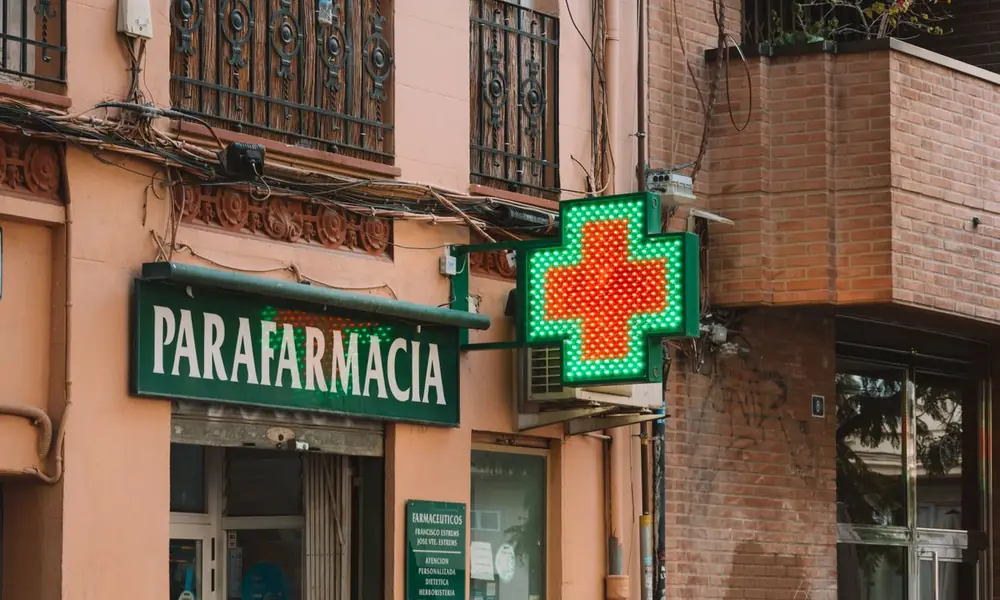 Fachada de una parafarmacia con su cruz luminosa encendida en una calle